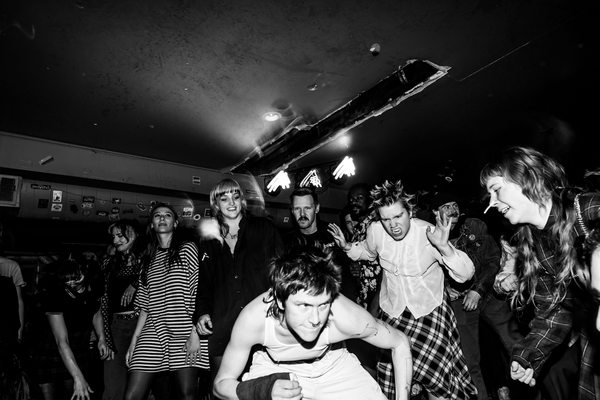 A black and white photo shows artist Jed Arbour crouching in front of an enthusiastic crowd during a live performance.