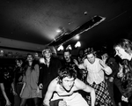 A black and white photo shows artist Jed Arbour crouching in front of an enthusiastic crowd during a live performance.
