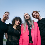 A colour fisheye photo taken from below shows four-piece band lushclot standing outside with a blue sky behind them.