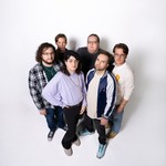 A colour photo taken from above shows six-piece group standing in a group against a white background.