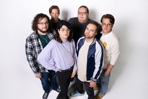 A colour photo taken from above shows six-piece group standing in a group against a white background.