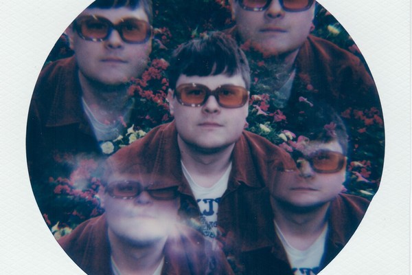 A colour kaleidoscope-type photo shows the front person of Pearly Moon from the shoulders up wearing orange glasses with flowers in the background. Because of the kaleiscope effect, there appears to be five of the same person