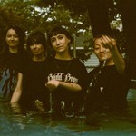 A grainy colour photo shows four-piece band Penny & the Pits standing waist deep in a outdoor pool of water.