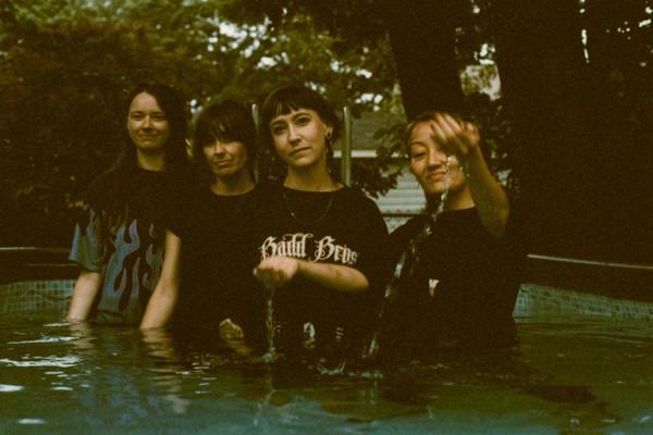 A grainy colour photo shows four-piece band Penny & the Pits standing waist deep in a outdoor pool of water.