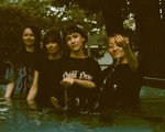 A grainy colour photo shows four-piece band Penny & the Pits standing waist deep in a outdoor pool of water.