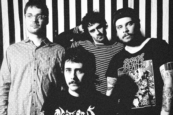 A black and white photo shows four-piece band Pnoon standing in front a black and white striped wall.