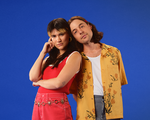 A bright colour photo shows the indie duo Pony Girl posing for a photo in front of a blue background. They're dressed in bright red and yellow clothes.