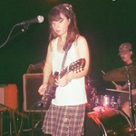 A faded colour photo shows three-piece group puppet wipes performing live with the guitar and bass player at the forefront, and then drummer in the back.
