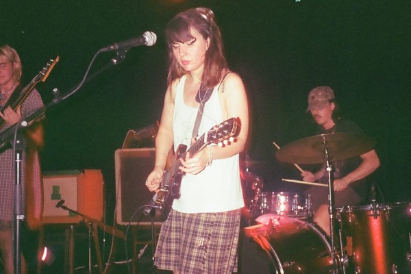 A faded colour photo shows three-piece group puppet wipes performing live with the guitar and bass player at the forefront, and then drummer in the back.
