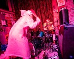 A colour photo shows two members of Radioactive Vampire Teeth bathed in red light performing upstairs at The Palomino. The frontperson is turned around hitting the drumkit. The drummer sits behind the kit.