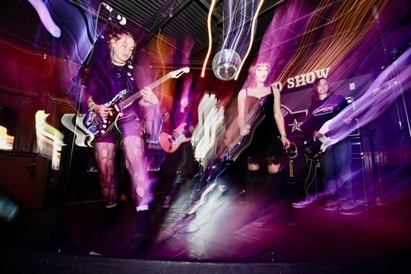 A long exposure colour photo shows five-piece punk band Rebel Grrrlz playing on stage at the Ship and Anchor.