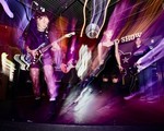 A long exposure colour photo shows five-piece punk band Rebel Grrrlz playing on stage at the Ship and Anchor.