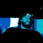 A blue and black photo shows artist SAMWOY singing into a microphone with a beard and sunglasses