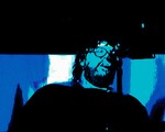 A blue and black photo shows artist SAMWOY singing into a microphone with a beard and sunglasses