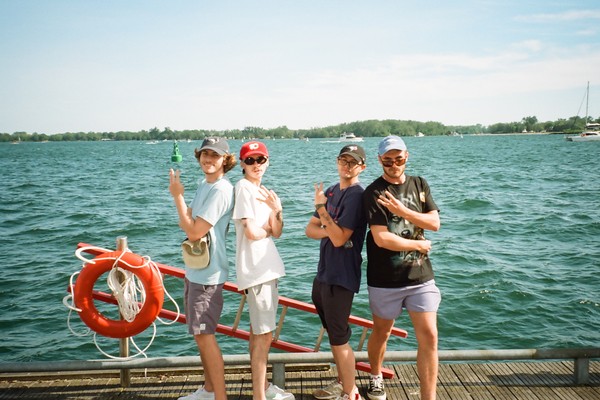 A colour photo shows four-piece band Sea of Lettuce standing on a wooden dock with a body of water behind them. 