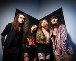 Four-piece band Shiv and the Carvers pose stand in a line and pose for a colour photo in the corner of a black and grey room