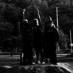 A dark black and white photo shows four-piece Spirit Desire standing outside all in black clothes. Two members raise their fists in the air.
