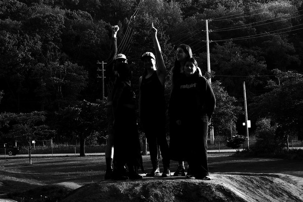 A dark black and white photo shows four-piece Spirit Desire standing outside all in black clothes. Two members raise their fists in the air.