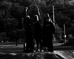 A dark black and white photo shows four-piece Spirit Desire standing outside all in black clothes. Two members raise their fists in the air.