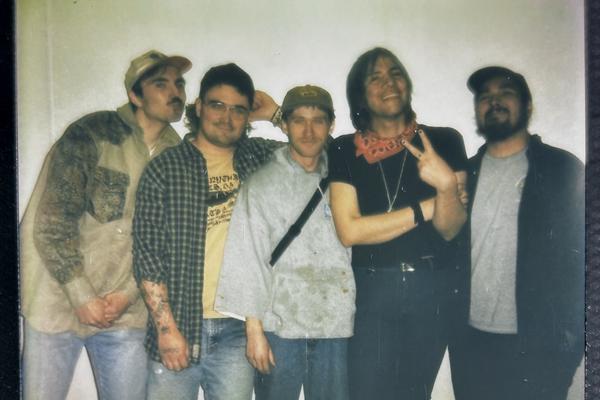 A slightly out of focus colour polaroid shows five-piece Spirit Hote smiling for a photo against a white wall.