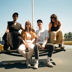 A colour photo of four-piece Stem Champ sitting on a picnic table in an empty outdoor parking lot with a clear blue sky behind them