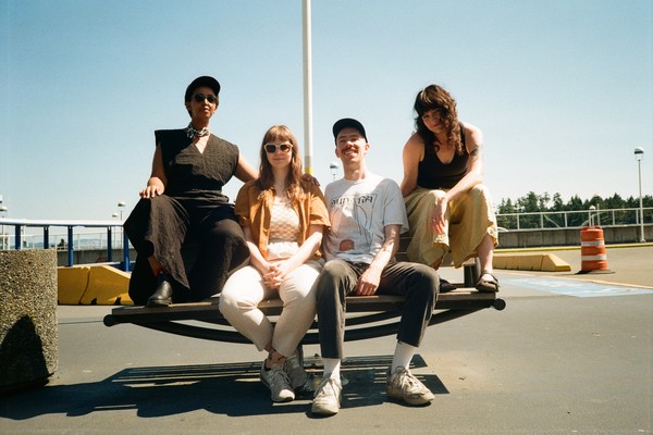 A colour photo of four-piece Stem Champ sitting on a picnic table in an empty outdoor parking lot with a clear blue sky behind them