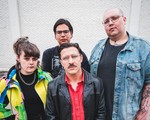 A colour photo of four-piece group Stucco shows them posing against a white brick wall.