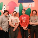 Four-piece band Temps pose for a colour photo against a pink wall featuring abstract art.