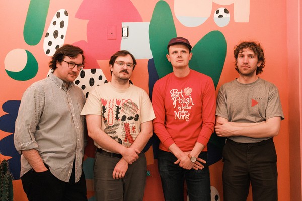 Four-piece band Temps pose for a colour photo against a pink wall featuring abstract art.