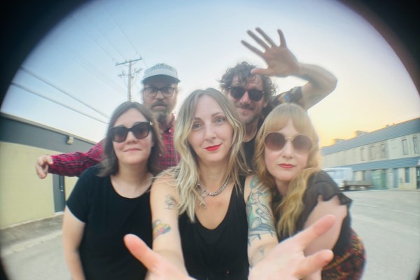 A colour fisheye photo of five-piece band The Radiation Flowers standing in a motel parking lot.