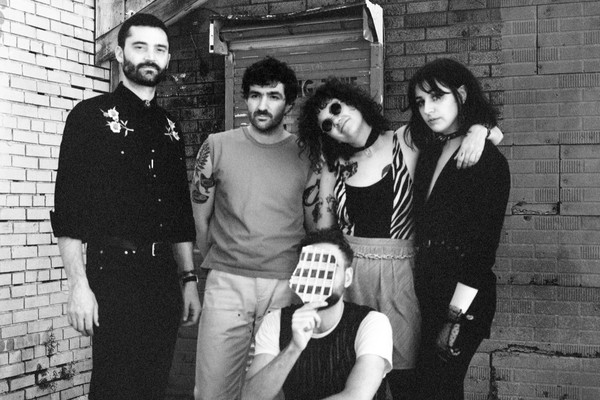 A black and white photo shows five-piece band Uncanny Valley posing in a back alley.