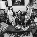 A black and white photo shows the three-piece band Window Lamp Corp posing on a couch