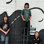 A colour photo shows three young members of the group Pollux posing in a parking lot.