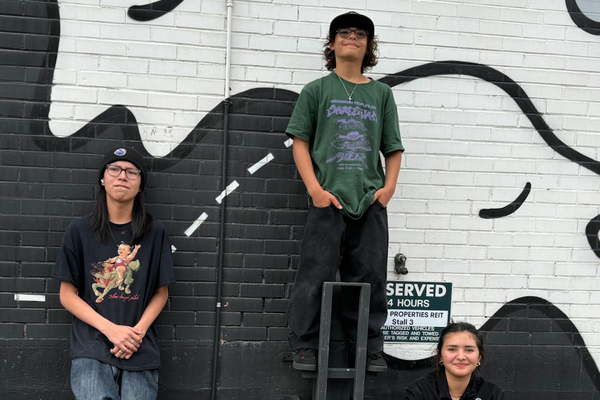 A colour photo shows three young members of the group Pollux posing in a parking lot.