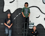 A colour photo shows three young members of the group Pollux posing in a parking lot.