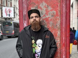 Outdoor portrait of comedian Tommy Mellor standing in front of a rustic telephone booth