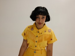 Portrait of comedian Isabel Zaw-Tun in a vibrant matching top and skirt, with a light neutral background behind her.