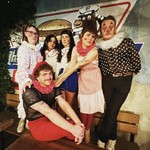 Six members of eclectic punk band Parisian Orgy are posed, standing on a bench while casually wearing clown attire