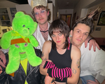 Photo taken indoors of eclectic four-piece Dial Up. One member is wearing a green teddy bear as a mask, another in bishop attire, one in black in pink striped hand warmers and the last with their hair spiked up.