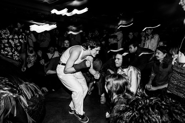 Black and white long exposure photo taken of the lead performer of Jed Arbour crouched toward an engaged crowd in a dimly lit venue.