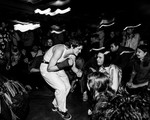 Black and white long exposure photo taken of the lead performer of Jed Arbour crouched toward an engaged crowd in a dimly lit venue.