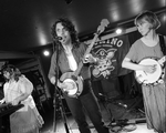Black and white photo taken of Bugswallow performing on stage at the Palomino. Front person is singing and playing steel guitar, image also contains a member playing banjo and one on keyboard.