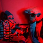 Double exposure photo washed in red light of the front person of Wheelchair Sports Camp holding someone in a leather jacket and sunglasses by the leash