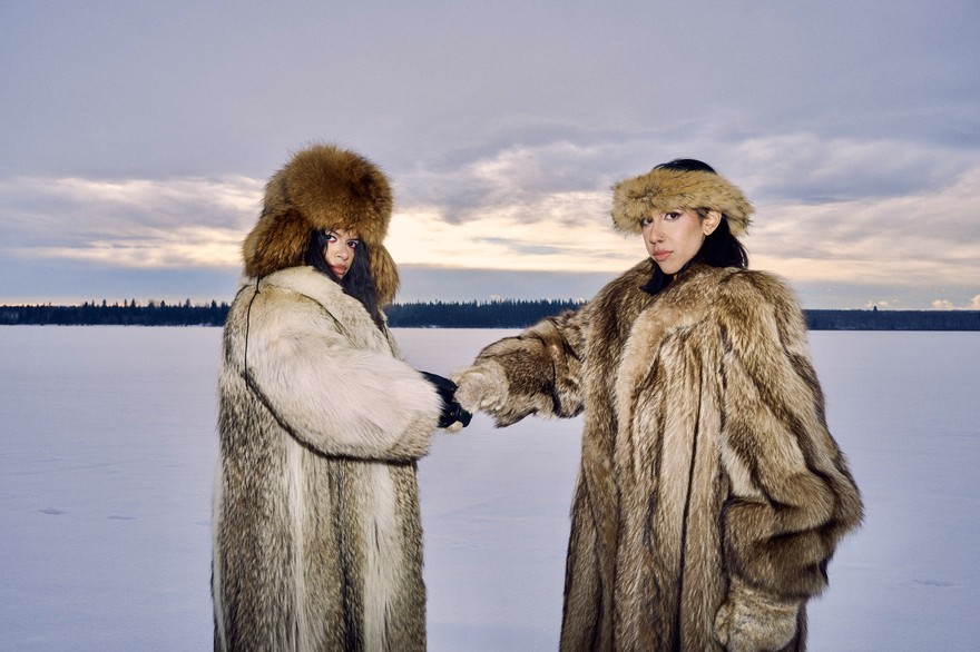 Duo Cartel Madras are posed in a vast snow covered terrain, both wearing heavy fur coats and hats.