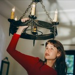Portrait of solo artist Emily Yacina reaching toward a chandelier.