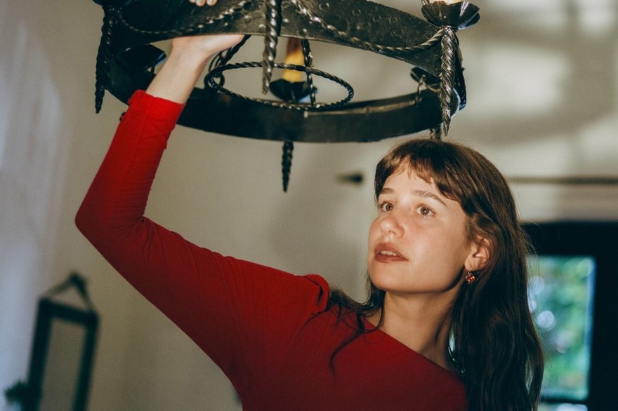 Portrait of solo artist Emily Yacina reaching toward a chandelier.