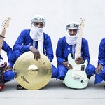 Photo of four-piece Etran de L'Aïr posed sitting with their instruments, each wearing traditional Nigerien wear