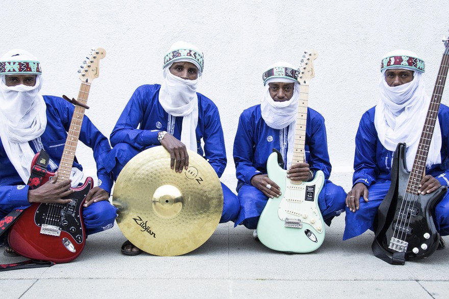 Photo of four-piece Etran de L'Aïr posed sitting with their instruments, each wearing traditional Nigerien wear
