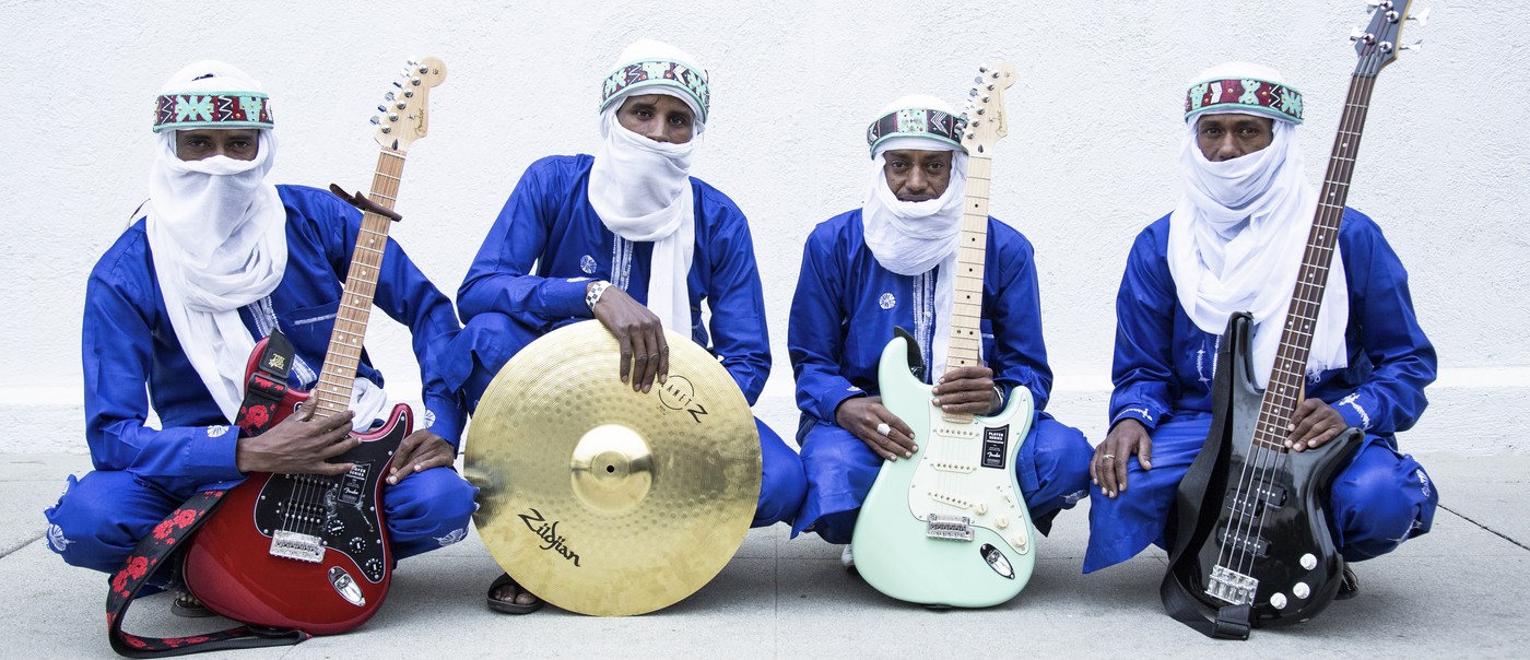 Photo of four-piece Etran de L'Aïr posed sitting with their instruments, each wearing traditional Nigerien wear