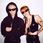 Duo Sextile are both in dark sunglasses, faced toward the camera, with a neutral background